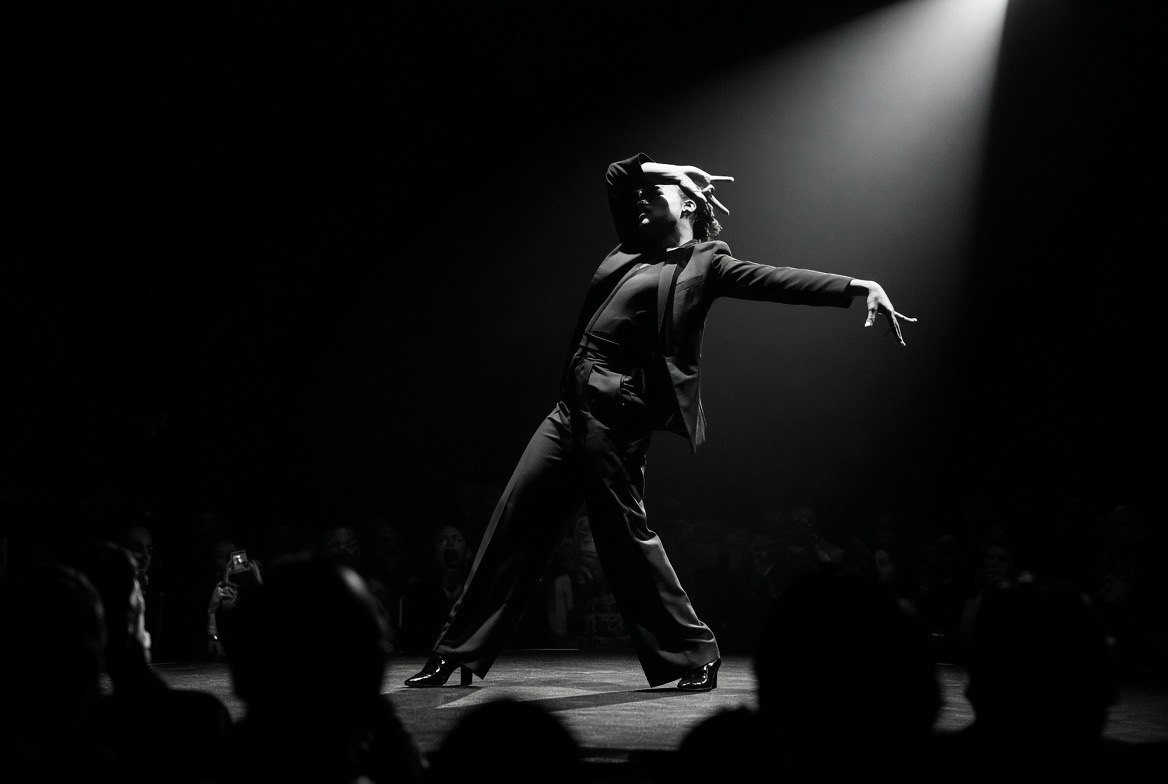 A performer striking a pose in a spotlight before a crowd